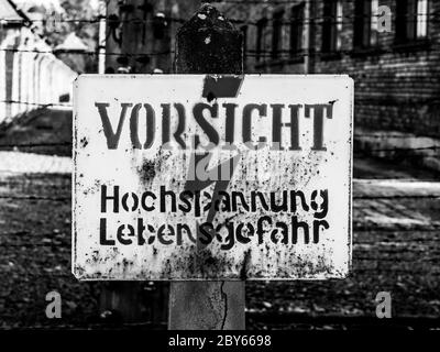 Cartello di allarme sul recinto elettrico nel campo di concentramento di Oswiecim, Polonia. Immagine in bianco e nero. Foto Stock