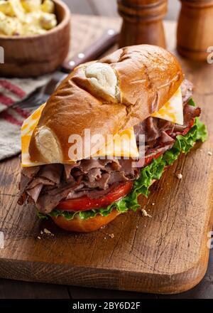 Sandwich sottomarino di manzo arrosto con formaggio, pomodoro e lattuga su un tagliere di legno Foto Stock