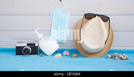 Alcuni accessori da spiaggia insieme a oggetti di protezione del coronavirus collocati su una tavola di legno. Spazio per il testo. Concetto di vacanze, estate e nuova normalità Foto Stock