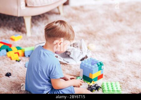 Little boy gioca con le auto del designer e giocattolo in una T-shirt blu sul pavimento Foto Stock