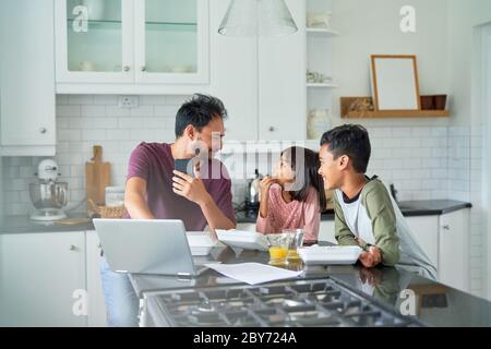 Padre che lavora in cucina con i bambini che mangiano cibo da asporto Foto Stock