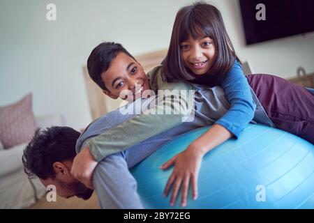 Ritratto giocoso bambini in cima al padre che si esercita sulla palla fitness Foto Stock