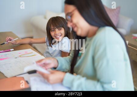 Felice ragazza colorazione accanto a madre pagando le fatture al tavolo da pranzo Foto Stock