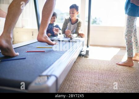 Bambini che gettano matite colorate sulla pedana mobile con il padre che fa jogging Foto Stock