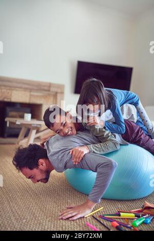 Bambini giocosi in cima al padre che si esercitano sulla palla di fitness Foto Stock