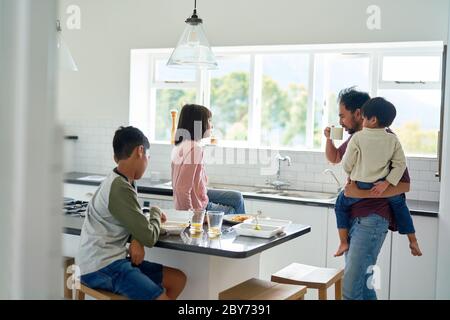 Padre e bambini mangiano cibo da asporto in cucina Foto Stock