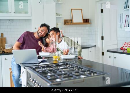 Il padre e i bambini giocosi mangiano e usano il computer portatile in cucina Foto Stock