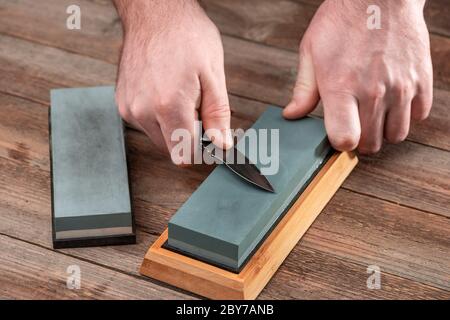 Uomo affilando il suo jackknife con una pietra su un tavolo rustico in legno Foto Stock