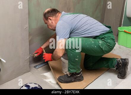 Ristrutturazione del bagno. Lavoratore di costruzione. Isolamento di umidità minerale. Durante il lavoro. Foto Stock