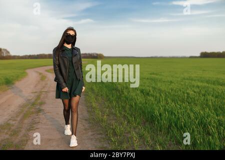 Una ragazza in una maschera medica corre o cammina su un campo verde. Quarantena primavera estate. Coronavirus. COVID 19. Virus influenzale, raffreddori Foto Stock