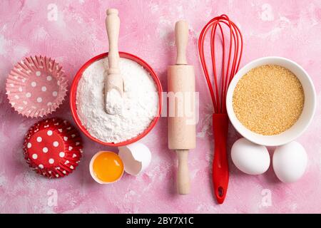 Ingredienti per la cottura - farina, uova, zucchero su fondo rosa. Cottura o cottura di torte o muffin. Vista dall'alto, disposizione piatta Foto Stock