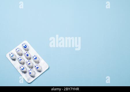 Blister di pillole divertenti con sorrisi volti su sfondo blu. Assistenza sanitaria, pillole giornaliere, antidepressivi, medicina, concetto di trattamento. Spazio di copia Foto Stock