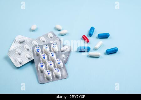 Blister di pillole divertenti con sorrisi volti su sfondo blu. Assistenza sanitaria, pillole giornaliere, antidepressivi, medicina, concetto di trattamento. Spazio di copia Foto Stock