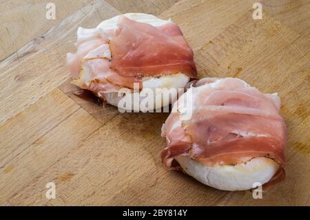 Tomino (delizioso formaggio di mucca piemontese) arrotolato con speck (prosciutto affumicato italiano) pronto per essere riscaldato prima della degustazione. Foto Stock