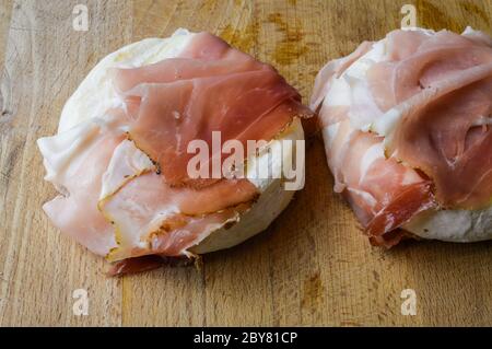 Tomino (delizioso formaggio di mucca piemontese) arrotolato con speck (prosciutto affumicato italiano) pronto per essere riscaldato prima della degustazione. Foto Stock