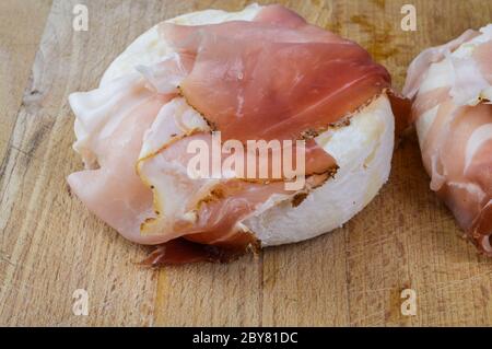 Tomino (delizioso formaggio di mucca piemontese) arrotolato con speck (prosciutto affumicato italiano) pronto per essere riscaldato prima della degustazione. Foto Stock