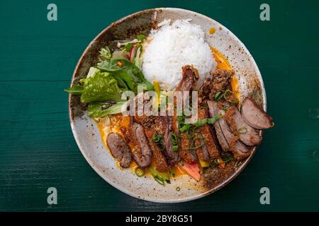 Chiudere la porzione di fettine arrostito croccante anatra alla pechinese curry con riso e insalata sulla piastra sopra il tavolo, elevati vista dall'alto, direttamente al di sopra di Foto Stock