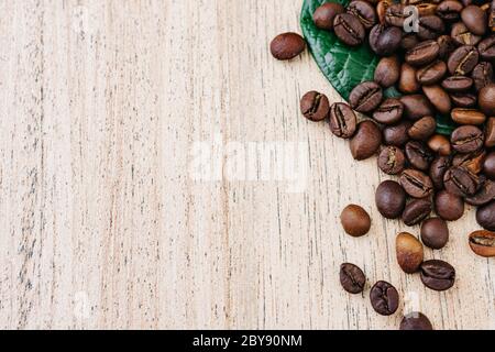 Caffè in grani su una foglia verde e sparsi su un tavolo di legno chiaro, fragranti fagioli fritti per americano fresco, espresso, sfondo naturale, vista dall'alto Foto Stock