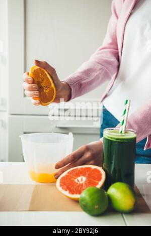 Donna caucasica spremitura di un succo d'arancia che si posa vicino a un bicchiere di bevanda naturale Foto Stock