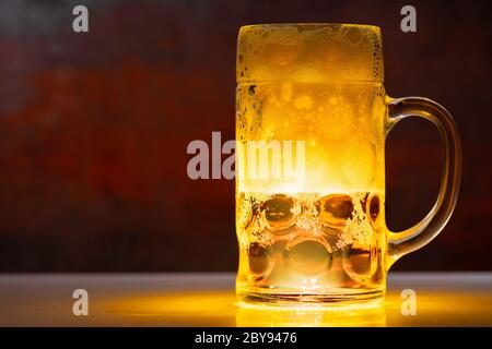 Mezza tazza di vetro piena di birra o lager con bolle effervescenti illuminate con luce su un banco bar o tavolo ombreggiato con copyspace Foto Stock