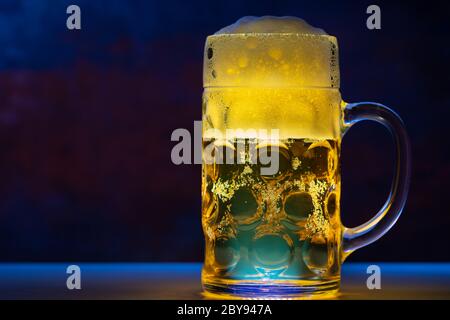 Tankard di vetro di birra chiara dorata su un bancone in luce blu con spazio di copia concettuale della vita notturna o di un club Foto Stock