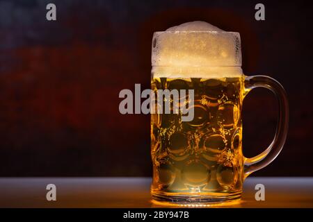 Tankard di birra con testa ghiacciata in una vista laterale ravvicinata su un bancone con spazio per la copia a lato illuminato da luce Foto Stock