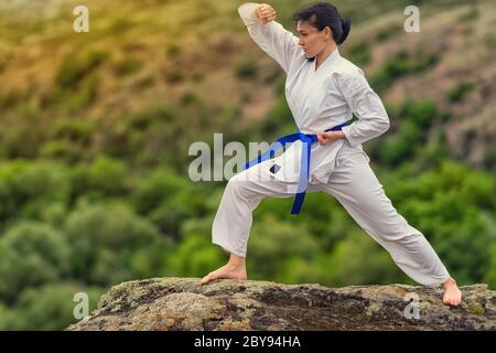 Giovane donna che pratica arti marziali o kickboxing all'aperto su una roccia che colpisce una posa in vista laterale contro il verde Foto Stock