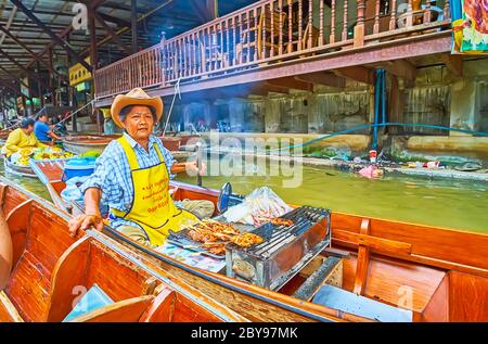 DAMNOEN SADUAK, THAILANDIA - 13 MAGGIO 2019: Il venditore anziano vende carne di maiale alla griglia su spiedini dalla barca di cibo sampan nel mercato galleggiante di Ton Khem, ON Foto Stock