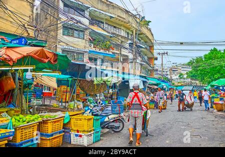 BANGKOK, THAILANDIA - 13 MAGGIO 2019: La strada trafficata del mercato della frutta Mahanak con molte bancarelle, che offre frutta fresca e facchini, a piedi con ruota-barr Foto Stock