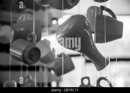 Foto monocromatica di silhouette di utensili da cucina. Vaso in ceramica, tazze da caffè e tazze da tè appesi a corde alla luce del sole. Caffè del mattino e. Foto Stock