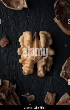Un kernel di noce su una superficie di legno nero con pezzi di Nuthell in pezzi Foto Stock