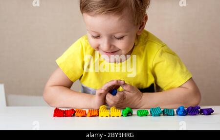 Caucasica baby bionda scolpisce da pasta per bambini per scolpire a casa al tavolo, bambini e creatività, lo sviluppo di belle capacità motorie. Foto Stock