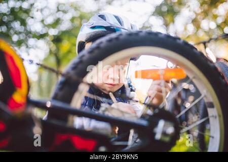 Attività di svago per bambini nel parco. Un bambino sta studiando il meccanismo di una mountain bike. Bambino che fissa una bicicletta nella foresta. Club ciclistico per Foto Stock