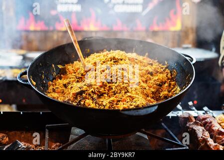 Pilaf caldo in grande calderone all'aperto. Cibo orientale tradizionale. Concetto di Street food. Primo piano Foto Stock