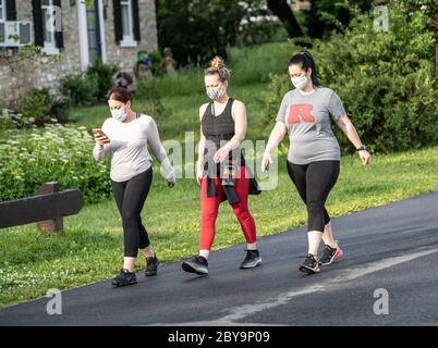 Berks County, Pennsylvania, USA - 3 giugno 2020: Tre giovani donne, indossando maschere di stoffa, camminando nel parco. Il CDC raccomanda a tutte le persone di indossare protezioni Foto Stock