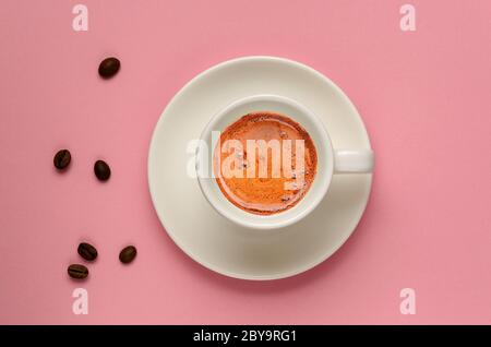 Creativa disposizione piatta di tazza di caffè bianca e alcuni chicchi di caffè su sfondo rosa millenario. Stile minimalista. Ma il caffè è il primo concetto. Spazio di copia Foto Stock