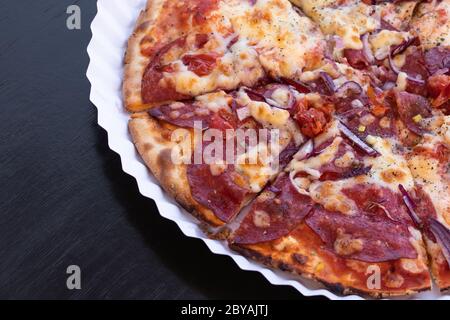 Fette di pizza con salame e formaggio su un piatto di carta. Tavolo di legno nero. Spazio di copia. Posizione vuota per il testo Foto Stock