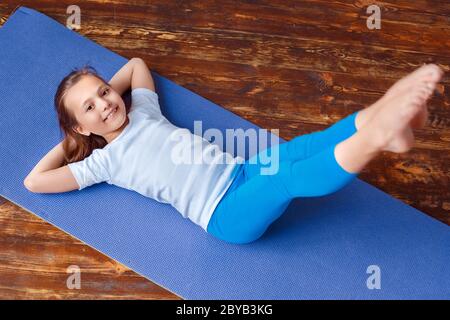 Stile di vita sano. Ragazza che fa yoga a casa su tappetino piegandosi giù gambe che si allungano sorridendo eccitato primo piano Foto Stock