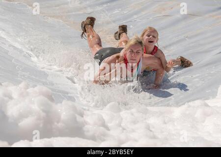 Poley Mountain, New Brunswick, Canada - 10 giugno 2017: Partecipazione alla raccolta fondi annuale 'mud Run for Heart'. Una donna e un bambino scivolano giù una schiuma Foto Stock