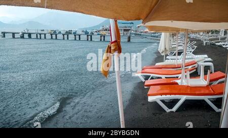 Lettini e ombrelloni bagnati sulla spiaggia durante la pioggia intensa Foto Stock