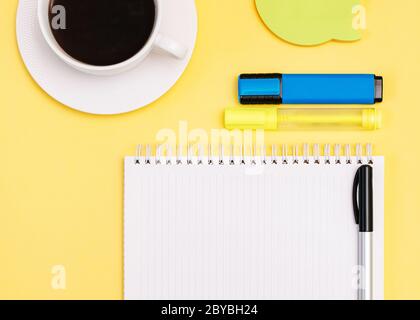 Notebook Vista dall'alto con spazio per la copia blocco note vuoto, forniture per ufficio e tazza di caffè nero su sfondo giallo Foto Stock