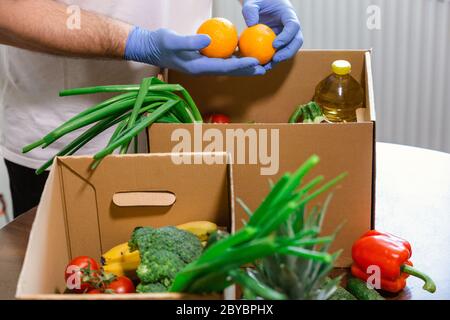 Fondi di soccorso e donazioni per il coronavirus. Volontari nella maschera medica protettiva e guanti per le mani Putting Food in Donation Box. Donazioni di beneficenza. Foto Stock