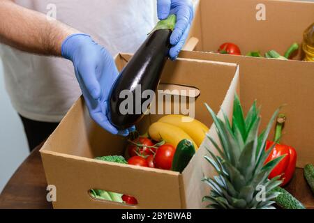 Fondi di soccorso e donazioni per il coronavirus. Volontari nella maschera medica protettiva e guanti per le mani Putting Food in Donation Box. Donazioni di beneficenza. Foto Stock