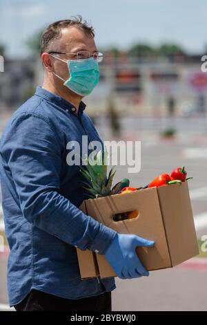 Uomo che consegna una scatola con cibo, uomo che consegna cibo in maschera protettiva e guanti Foto Stock