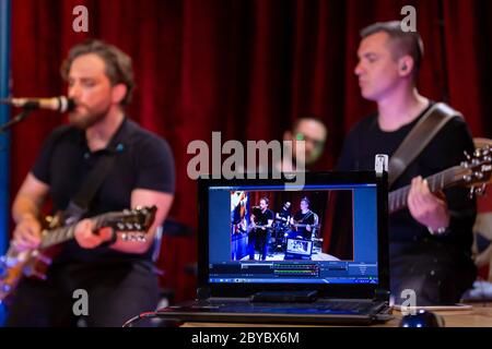La band di musicisti che suonano chitarra elettrica, basso e batteria durante il Concerto ha trasmesso on-line su piattaforme di social media nel Bar. Foto Stock