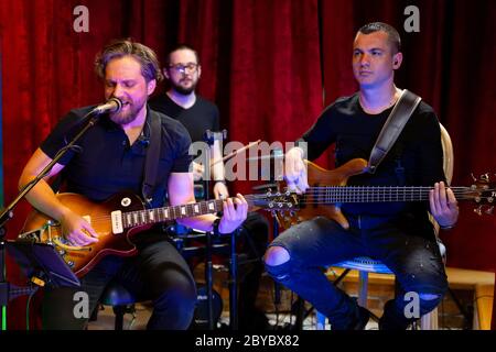 La band di musicisti che suonano chitarra elettrica, basso e batteria durante il Concerto ha trasmesso on-line su piattaforme di social media nel Bar. Foto Stock
