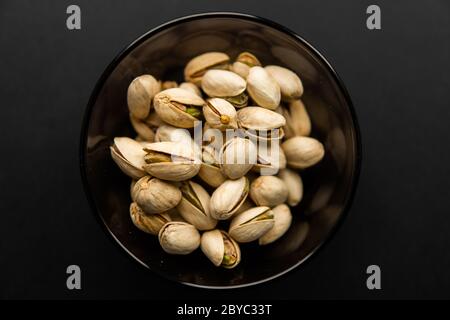 Pistacchi in un piccolo piatto su un tavolo nero. Il pistacchio è un alimento nutriente sano vegetariano della proteina. Spuntini naturali alla frutta secca. Foto Stock