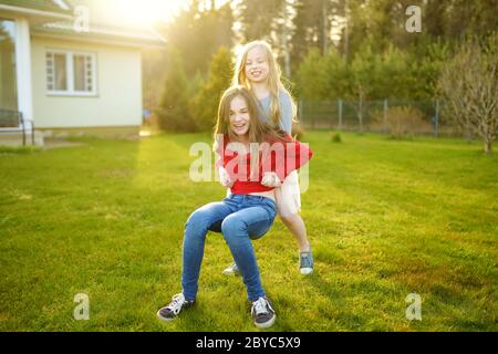 Due graziosi sorelle ingannare intorno insieme sull'erba su una soleggiata giornata estiva. I bambini di essere sciocco e divertirsi. Tempo per la famiglia. Foto Stock