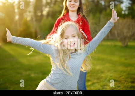 Due graziosi sorelle ingannare intorno insieme sull'erba su una soleggiata giornata estiva. I bambini di essere sciocco e divertirsi. Tempo per la famiglia. Foto Stock