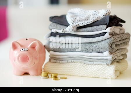 Un mucchio di vestiti del bambino, monete e una banca del piggy. Concetto di spese parenting. Elaborazione di un budget per i bambini. Risparmio di denaro quando si pianifica un neonato. Sporgenza Foto Stock